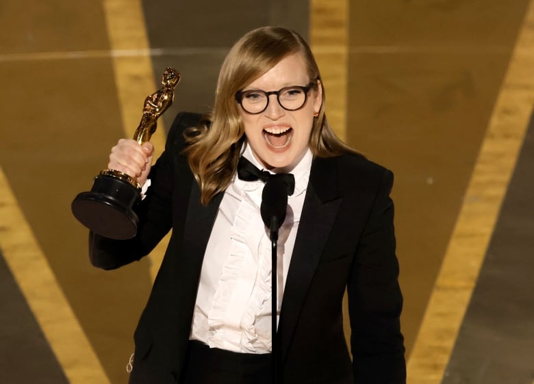 A smiling woman holds an Oscar statue.