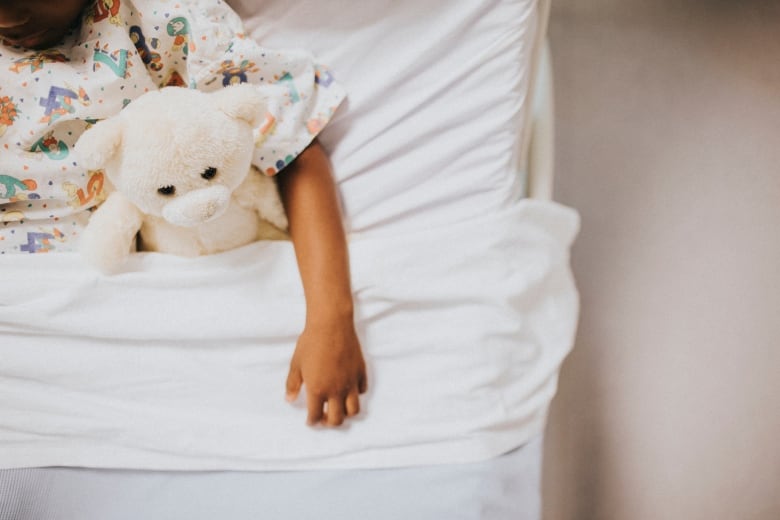 Bed with white sheets and little girl inside holding a stuffed animal