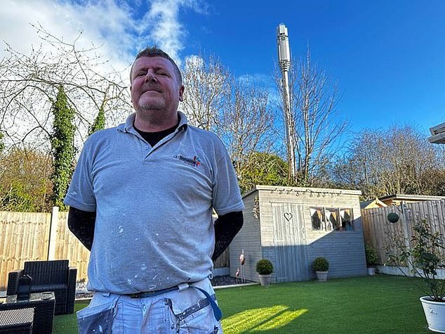 The angry householders of Eden Close in Shrewsbury, Shropshire have protested against the large mast. Pictured: An angry resident posing in a garden in front of the large mast