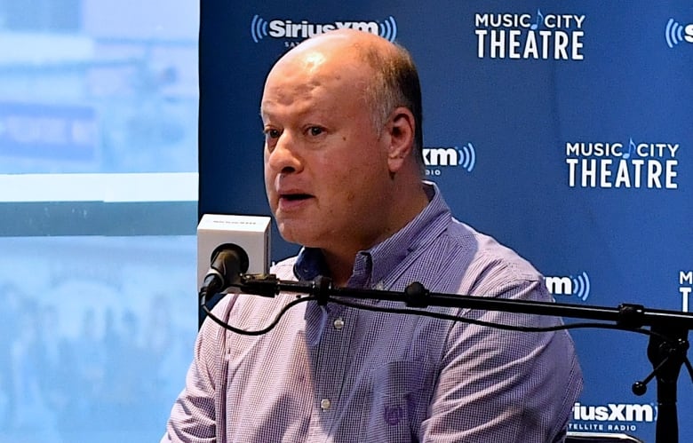 A man and a woman seated on chairs speak into microphones inside a radio studio. 