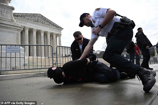 Early on in the bout, the man in the red shirt can be heard yelling: 'Knife! Knife!" as a police officer gets the man in the mask under control