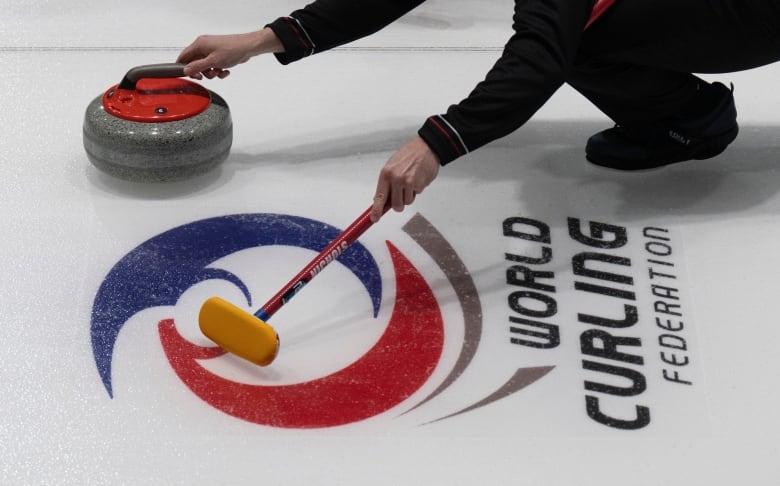 A man releasing a curling rock at a curling rink.