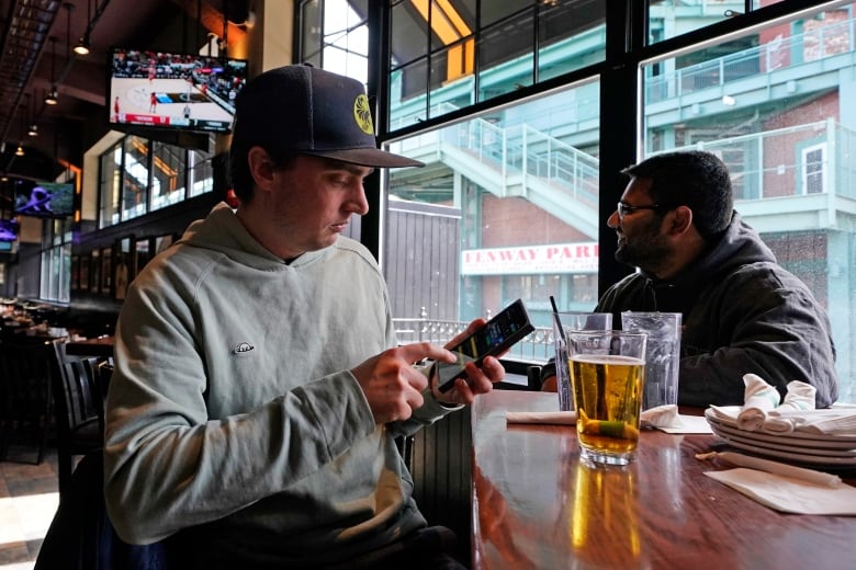 A man looks at a betting app on a phone, while sitting at a Boston sports bar.