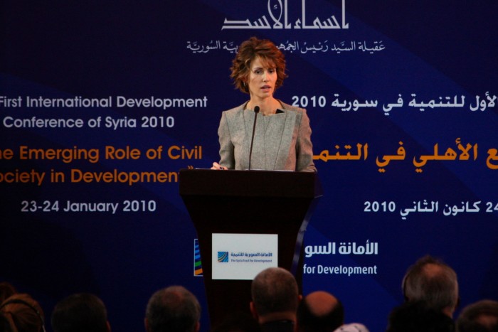 A woman in a grey suit speaks at a podium