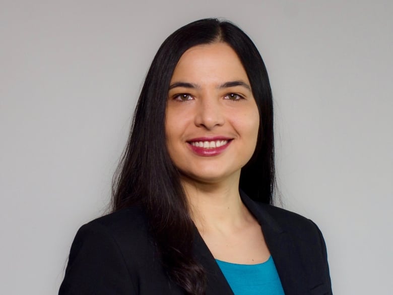 A woman with long dark hair smiles for a portrait while wearing a black blazer.