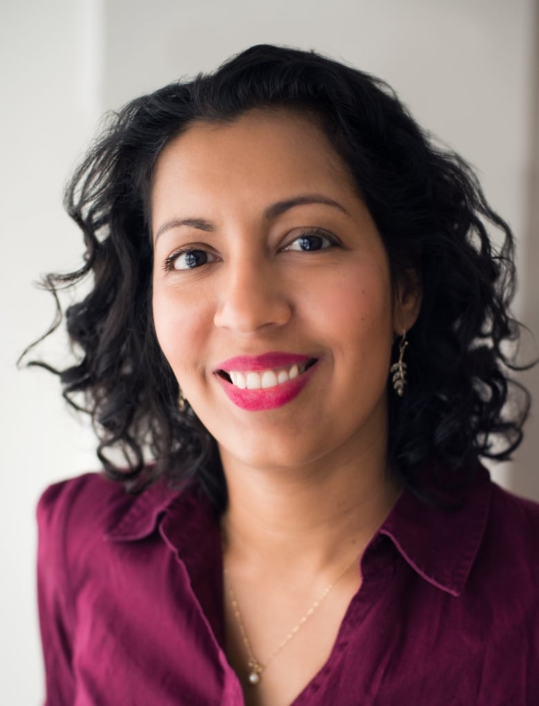 A woman with curly dark hair wearing a burgundy shirt smiles for a portrait.