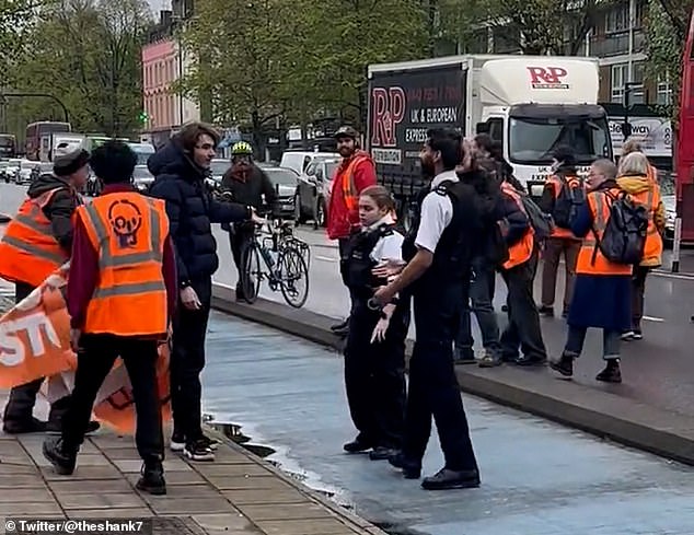 Today, police officers confronted another man (pictured in black, left) and told him to stop interfering with protesters