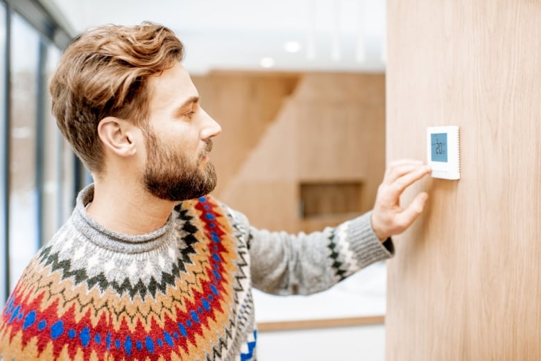 A man in a sweater adjusts the thermostat