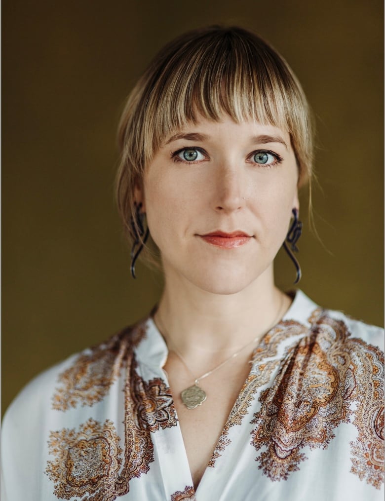 A woman in bold earrings and a patterned white and brown paisley top poses for a portrait.