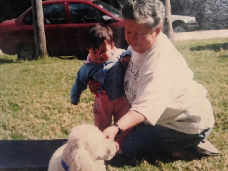 An older woman holding a baby and playing with a dog.