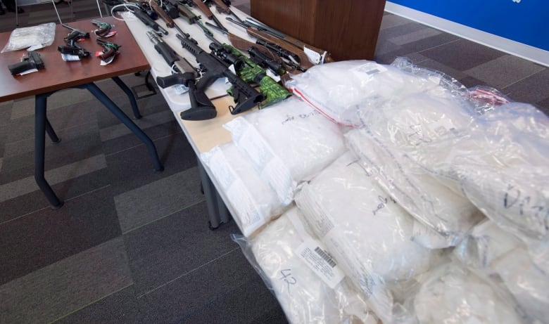 Illegal drugs and firearms lay on a table in front of a podium during a press conference.