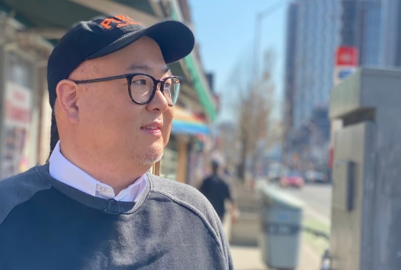 A man wearing a baseball hat and glasses stands outdoors.