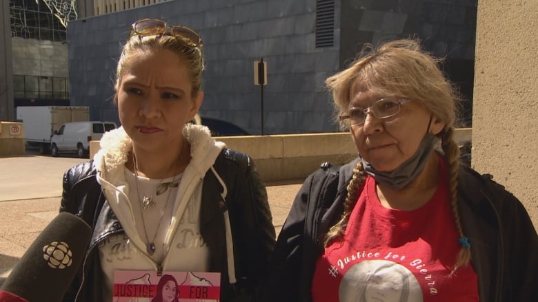 Two women in red stand side by side. The woman on the left has long braids.