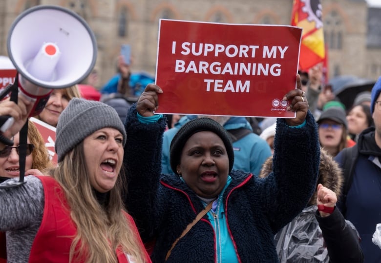 A striking public servant holds up a sign that reads "I support my bargaining team."