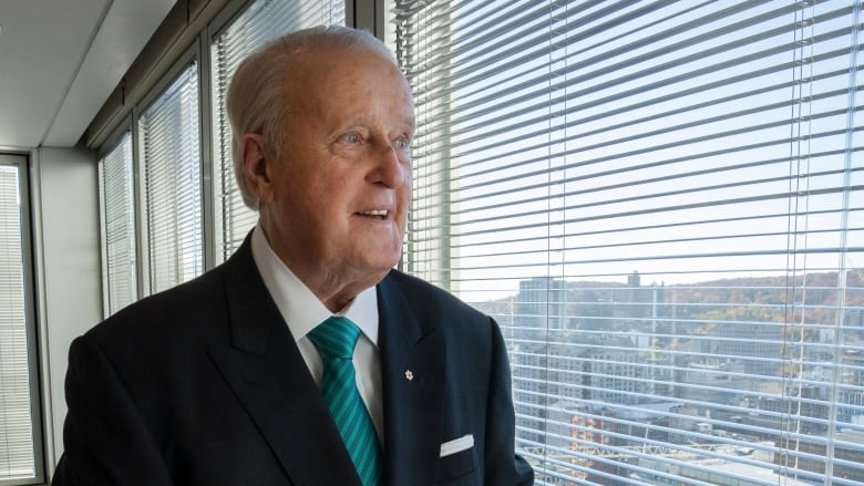 Older man looks out window in office building.