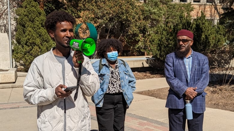 Organizers Ali Abukar, left, and Delilah Kamuhanda, centre, speak at the rally in front of Saskatoon City Hall on Saturday.