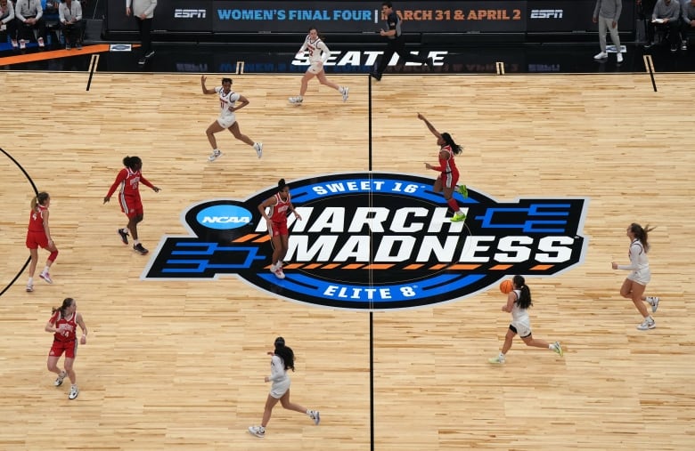 The March Madness logo is seen on a basketball court as women basketball players run during a game.