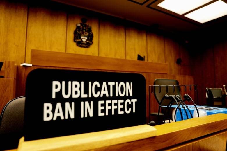 A sign saying "publication ban in effect" sits on a bench in a courtroom.