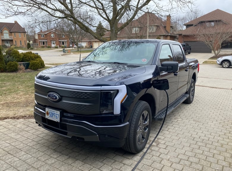 A black pickup truck sits in a brick-paved driveway, plugging into an electric charger.