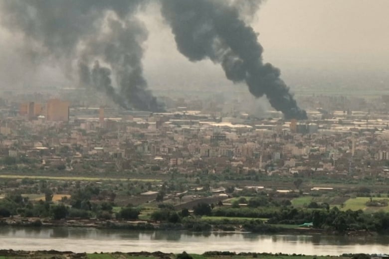 Two large black plumes of smoke rise above an urban vista.