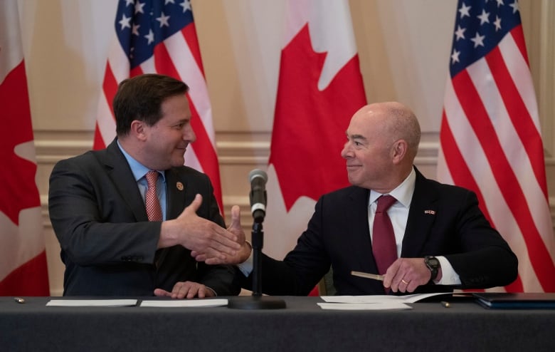 Two men in suits shake hands after signing documents.