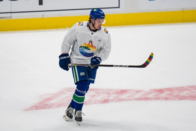 A male ice hockey player holds his stick at waist level with both hands while skating.