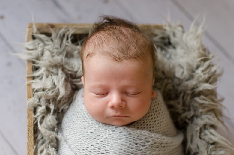 An eight week old baby lies swaddled in grey in a cradle.