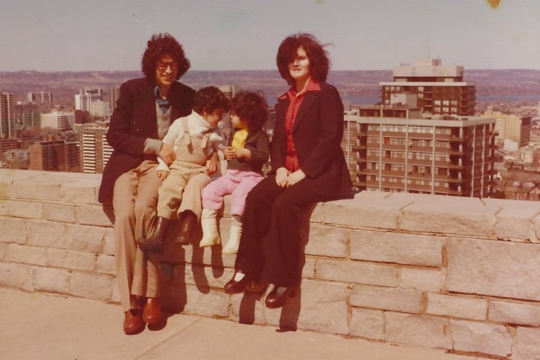 An old photo of a man, two children and a woman sitting on a wall.