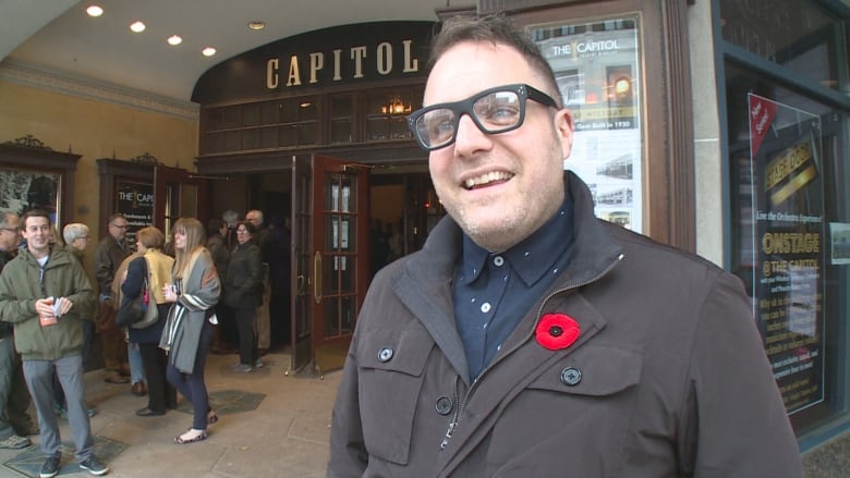 A man stands in front of a movie theatre.