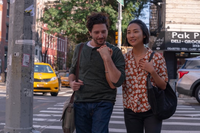 A man, left, and a woman smile and hold hands as the walk down a city street on a bright sunny day. 