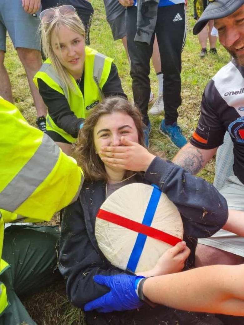 A woman looks excited holding a wheel of cheese.