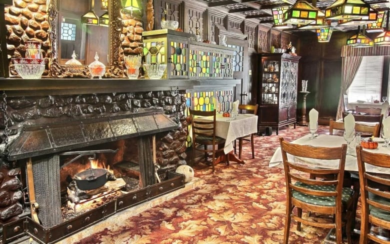 The interior of a restaurant with a fireplace and tables covered in linens.