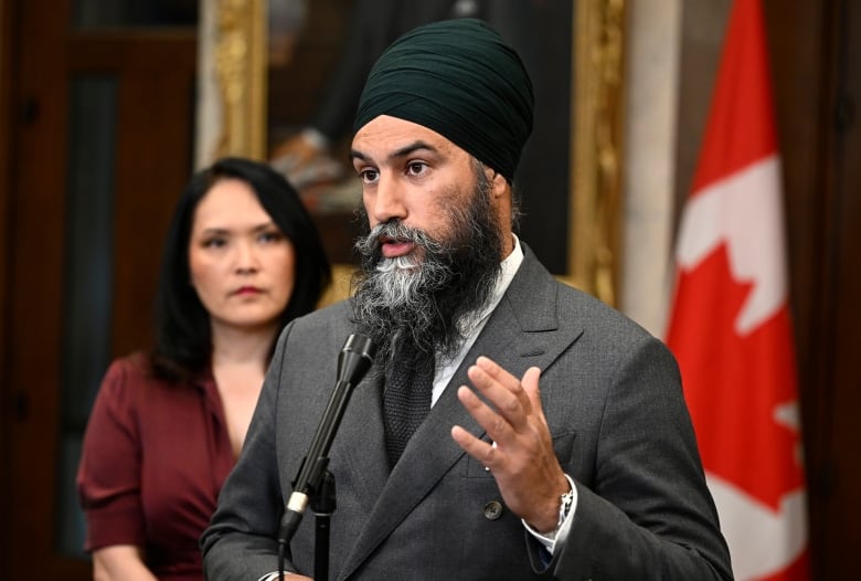 A man in a gray suit answers reporters' questions outside the House of Commons.