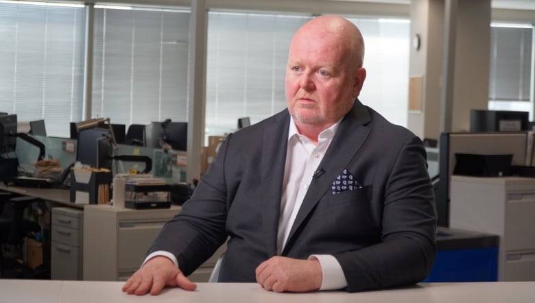 A man sits at a desk while being interviewed.