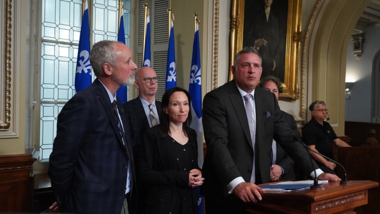 Politicians at a podium with Quebec flags in the background