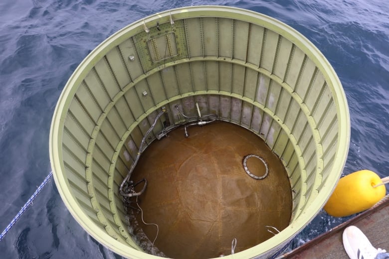 A hollow cylindrical object floats in a body of water.