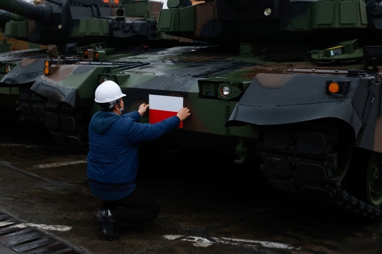 A worker fixes a Polish flag to a tank.