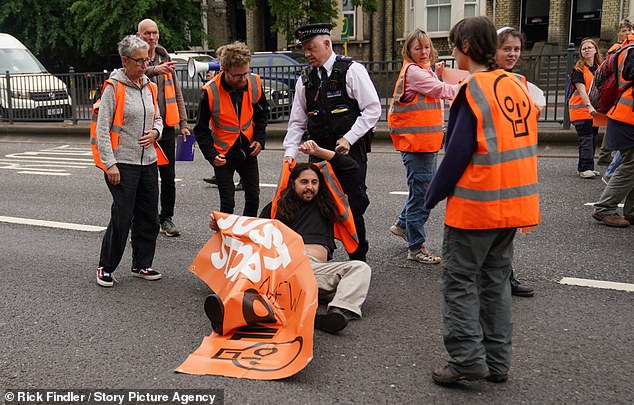 Policeman pushes and drags Just Stop Oil protesters out of the way while motorists blare horns