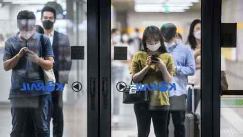 Commuters stand behind a glass safety barrier as they wait for their underground metro train in Seoul