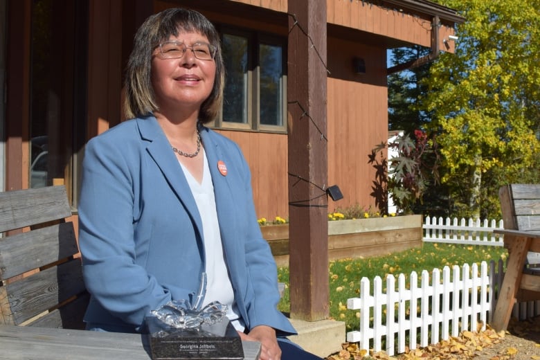 Woman posing for photo while grinning in front of a wooden home