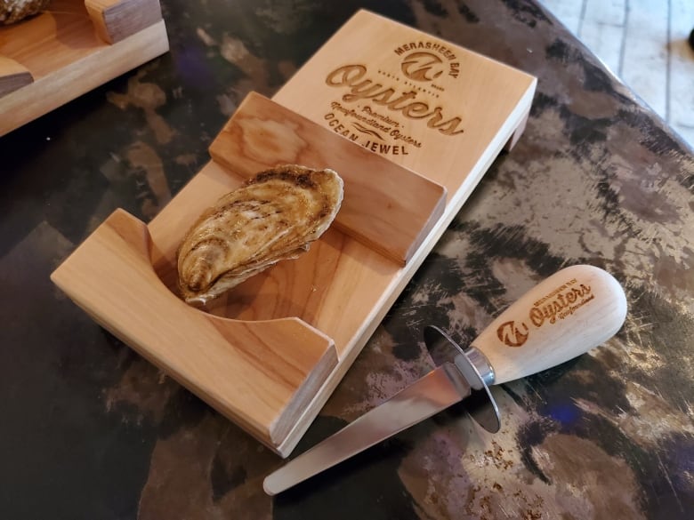 A Merasheen Bay Oyster is pictured on a shucking board, along with an oyster knife. 