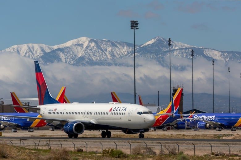 A Delta commercial airplane on a tarmac with snowcapped mountains on the horizon behind it. 