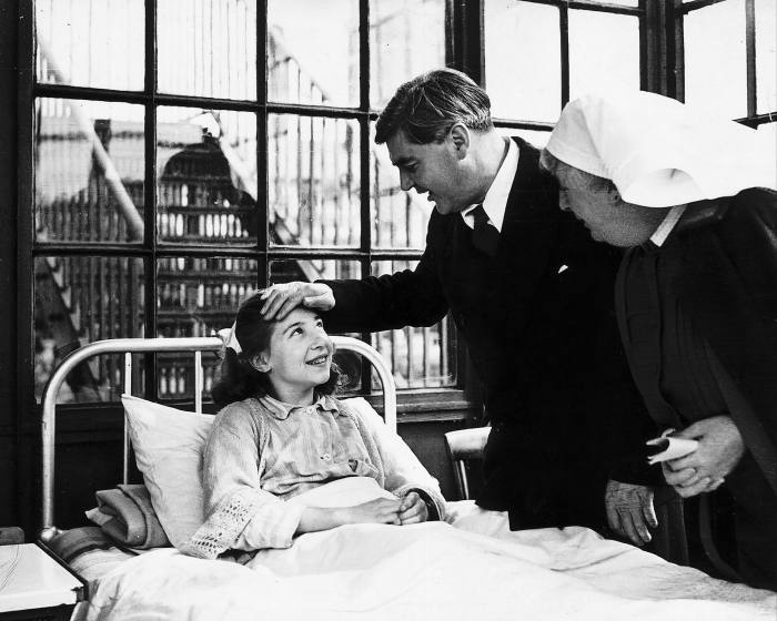 A man places his hand on a child’s head while a nurse looks on 