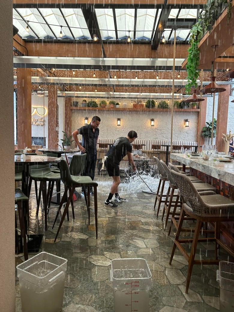 Two men in black shirts mop the floor in a restaurant. 