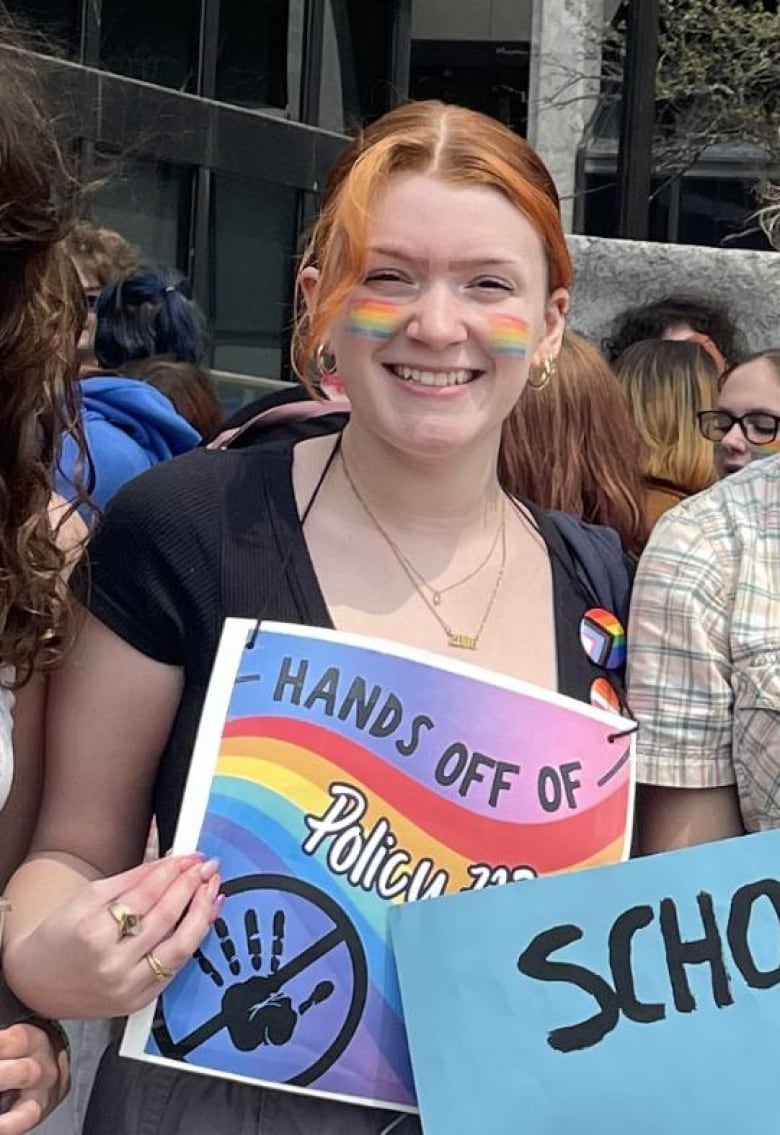 Three teens hold colourful signs at a rally.