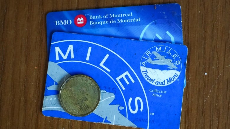 A close-up of a loonie dollar coin on an Air Miles card, placed on top of a BMO card.