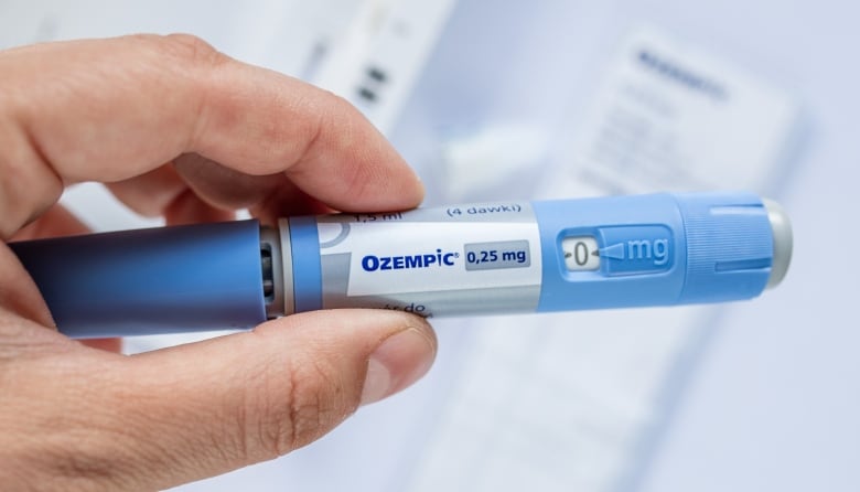 A blue needle with the brand name "Ozempic" on the side is pictured in a man's hand.