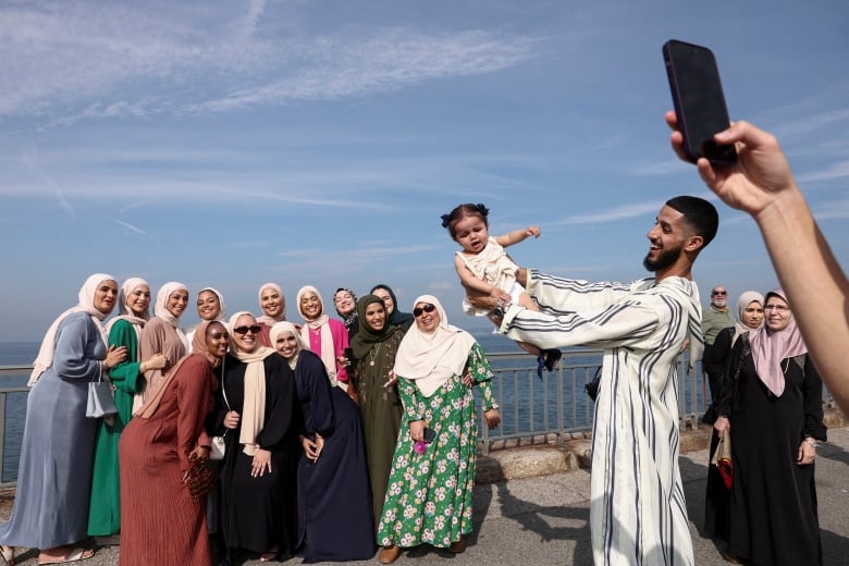 A man holds a baby near a group of women taking a picture during EId in NYC.