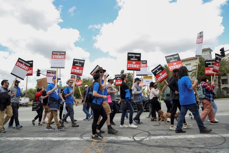 Striking workers carry signs as they walk on a picket line.