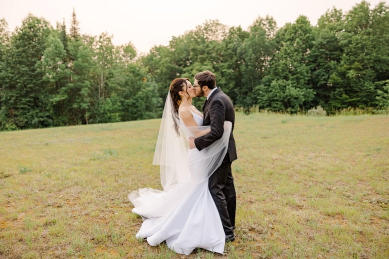 A man in a suit kisses a woman in a wedding dress in a field.